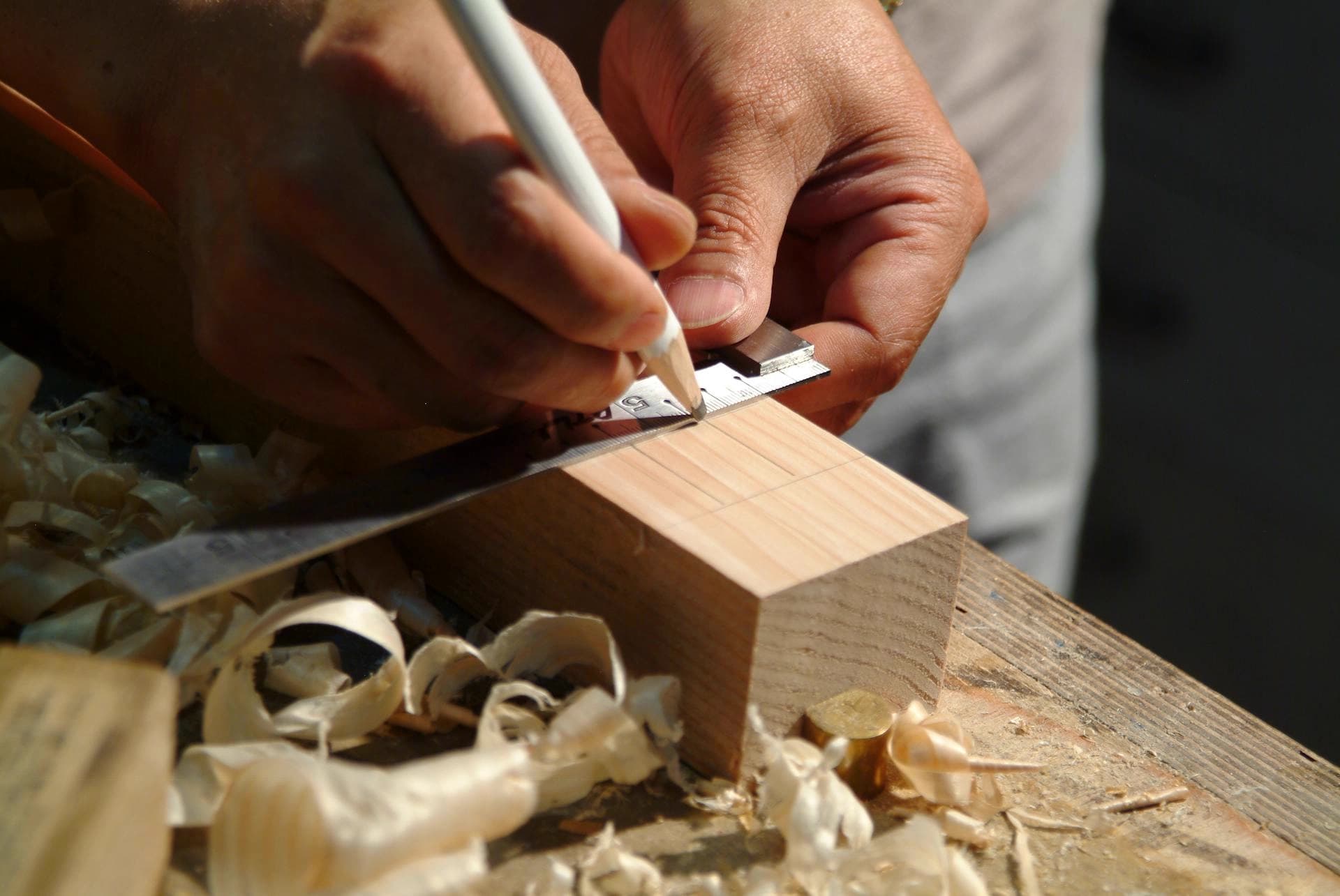 Close-up of hands using a pencil and ruler to carefully mark measurements on a piece of wood, representing Cabinet Connection's craftsmanship